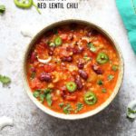 A bowl of instant pot red lentil chili on a white background with a turquoise napkin