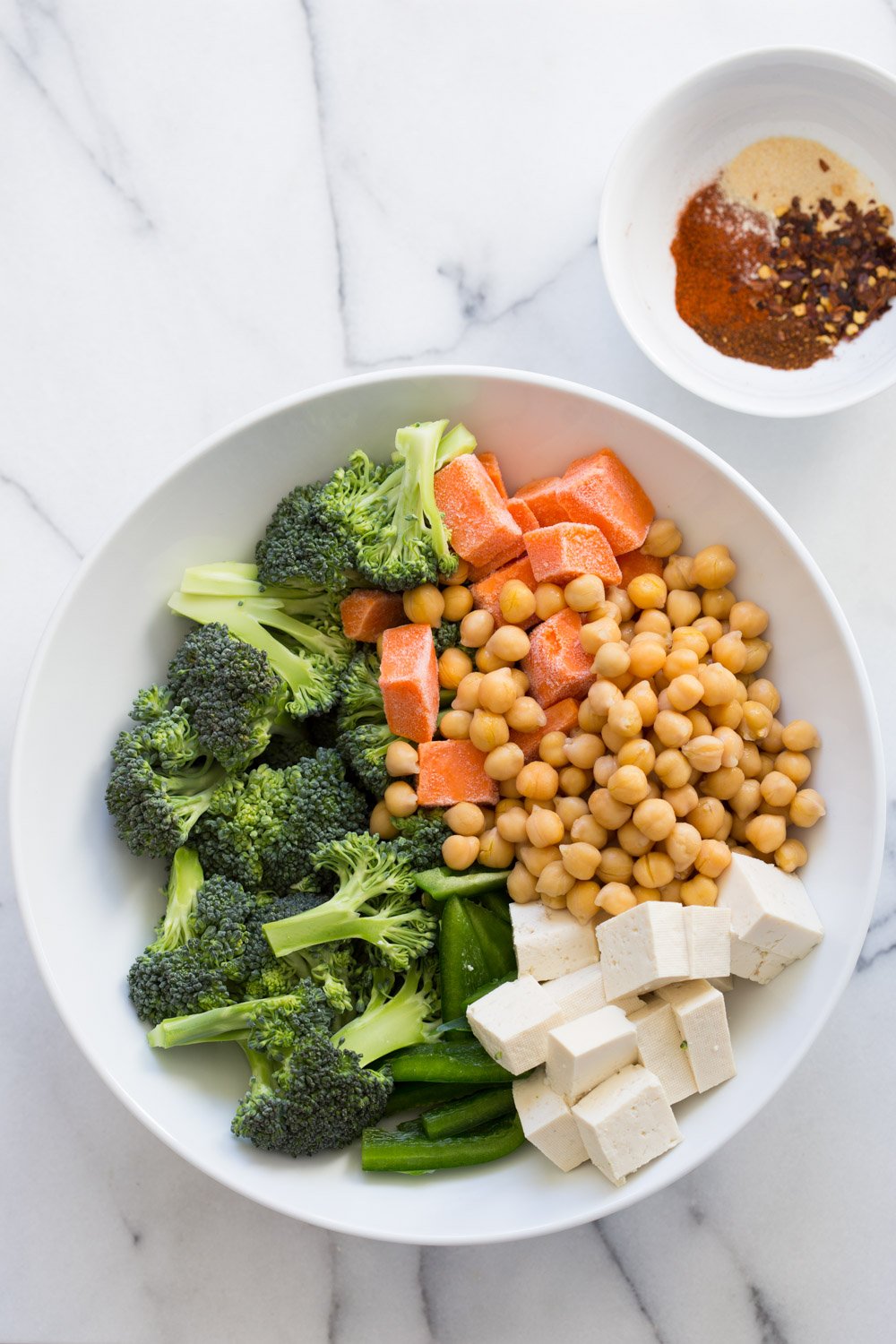 Chickpeas, Tofu, Broccoli, Sweet Potato in a White Bowl with spice bowl on the side