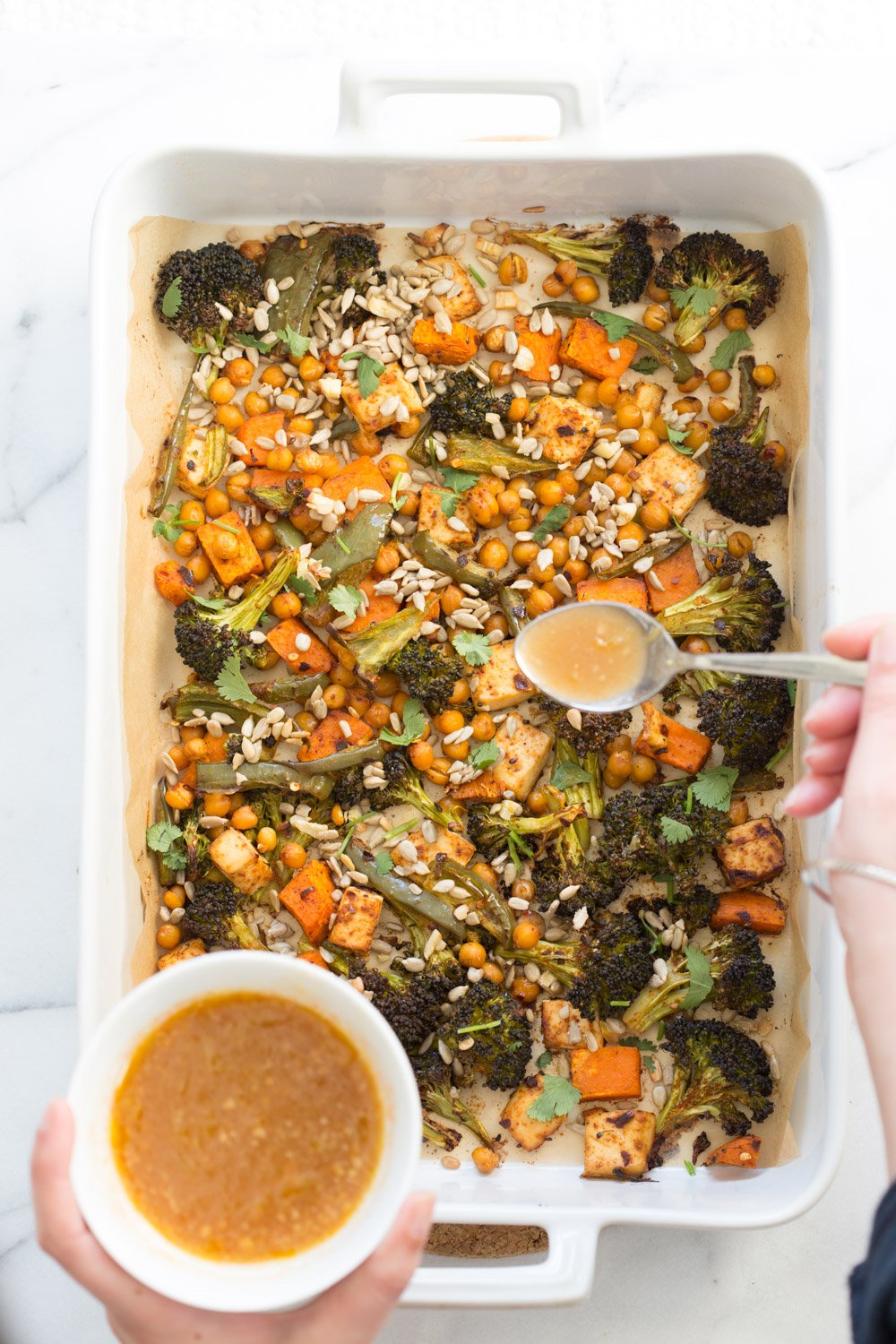 Roasted Veggies in a white Baking dish, getting dressed in miso maple dressing for Sheet Pan Veggie Dinner