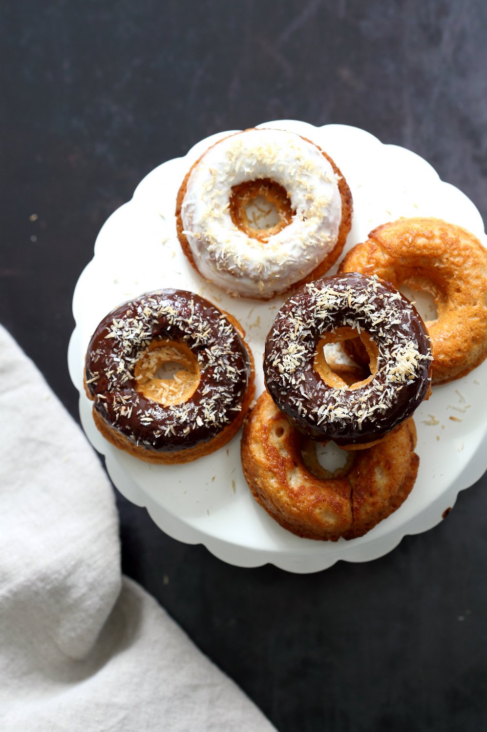 Vegan Banana Donuts with vanilla and chocolate icing on white cake stand