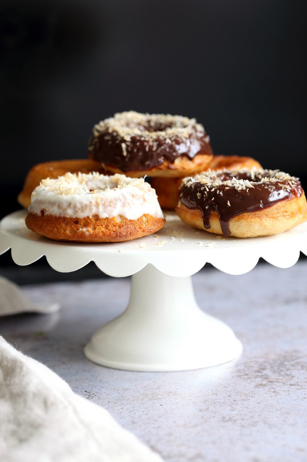Vegan Banana Donuts with vanilla and chocolate icing on white cake stand
