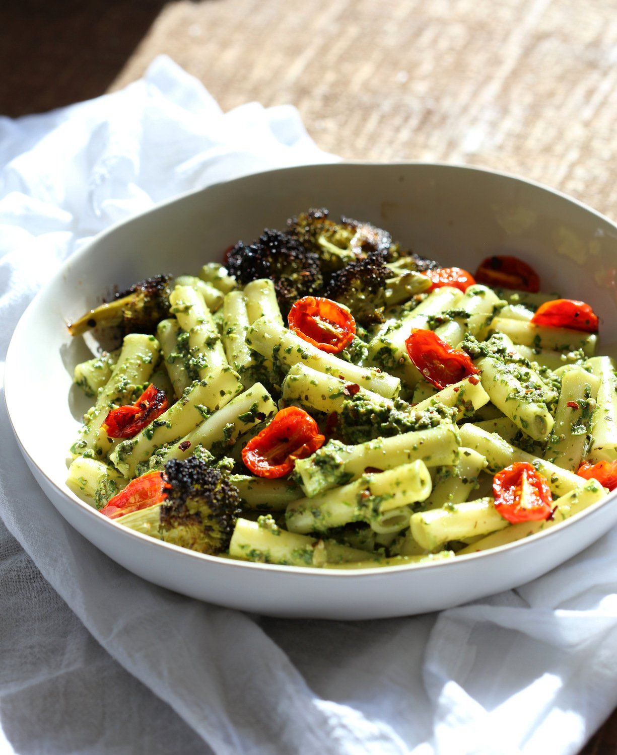 Large While Bowl with Vegan Pesto Pasta with Ziti, roasted cherry tomatoes and Charred broccoli on wood table