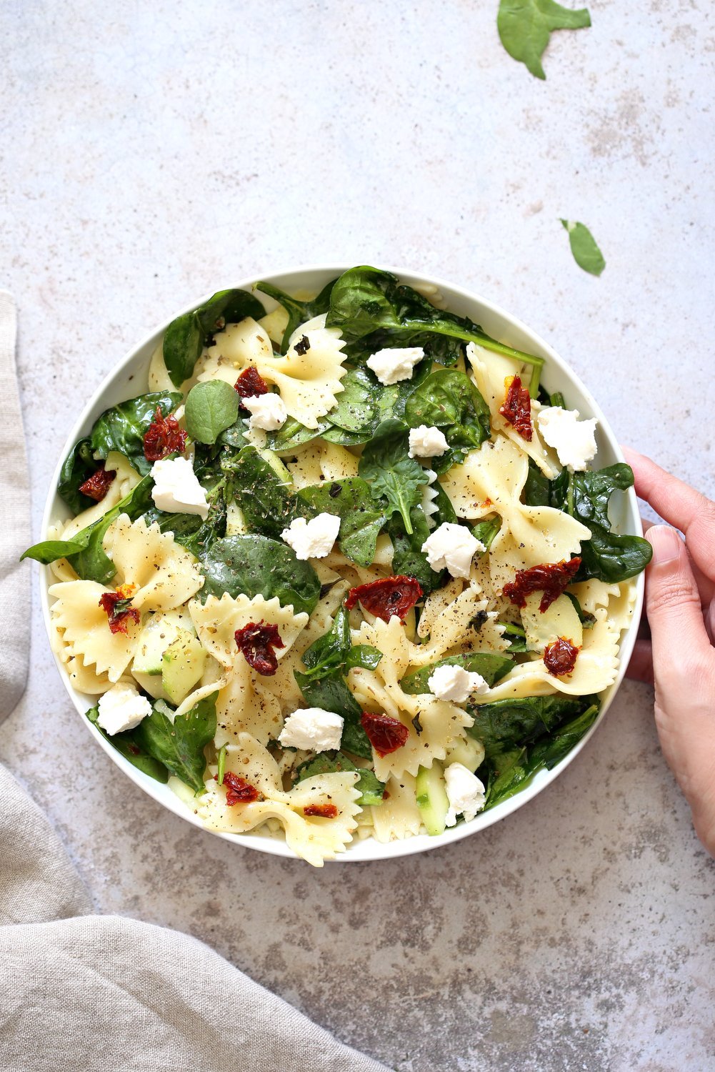 Tuscan Pasta Salad with sun dried tomato, cucumber, spinach, vegan feta in a White Bowl over Concrete