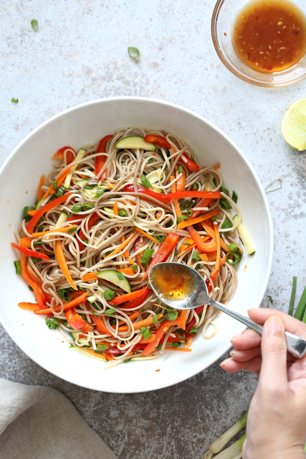 Our Cold Soba Noodle Salad in white Bowl getting dressed with Sesame Ginger Dressing