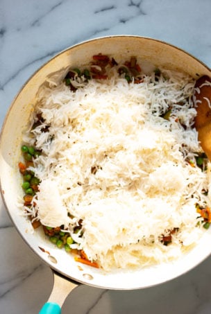 Cooked rice being added to the vegetables in a frying pan