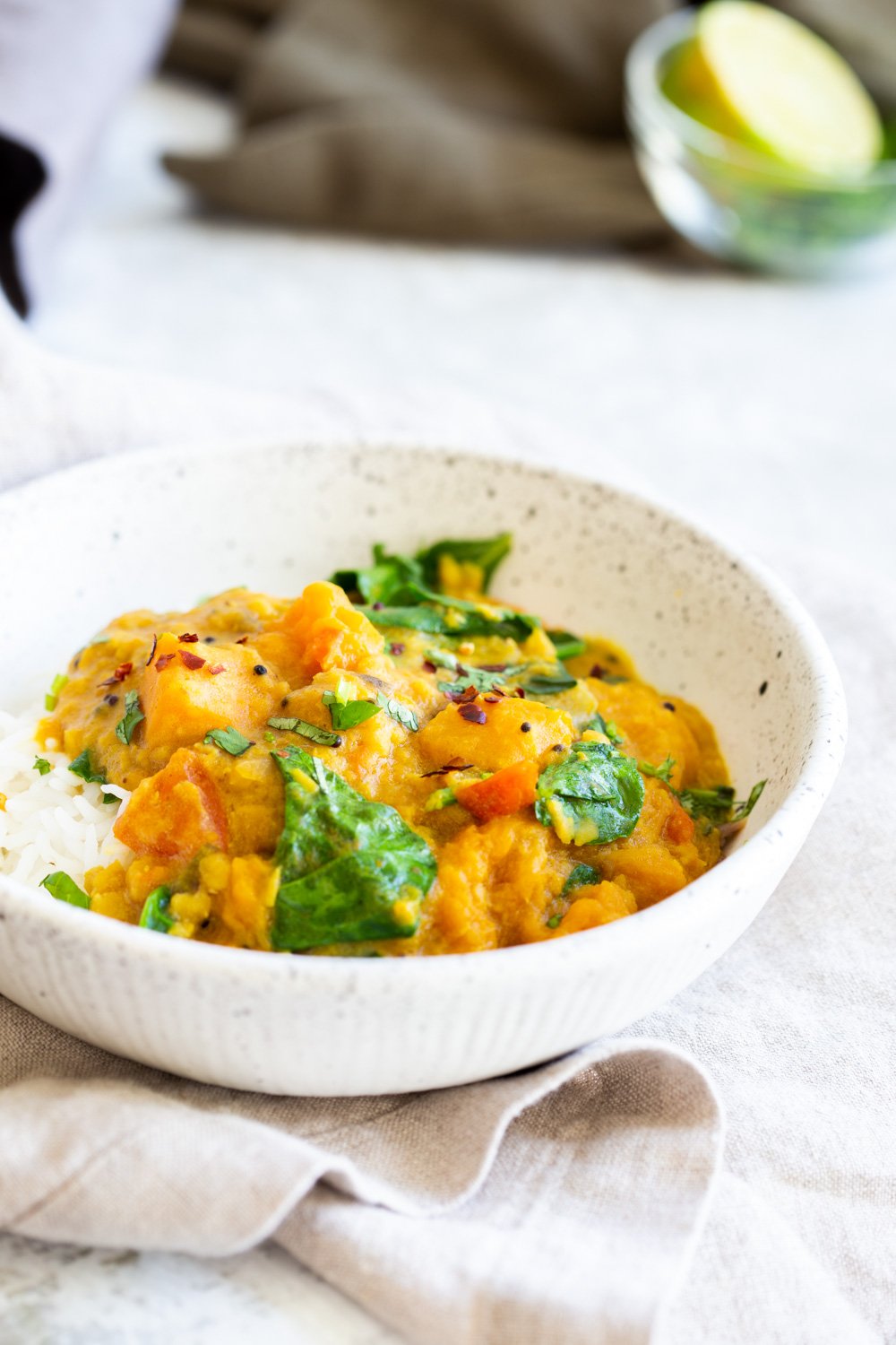 Instant Pot Red Lentil Butternut Squash Curry in a white speckled bowl kept on grey napkin