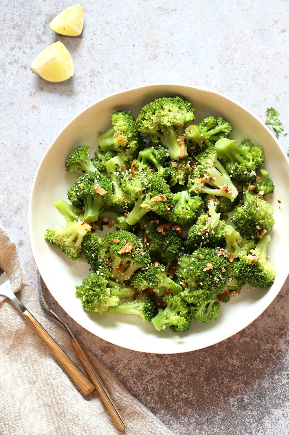 Sesame Garlic Broccoli garnished with sesame seeds in a white bowl with forks on the side