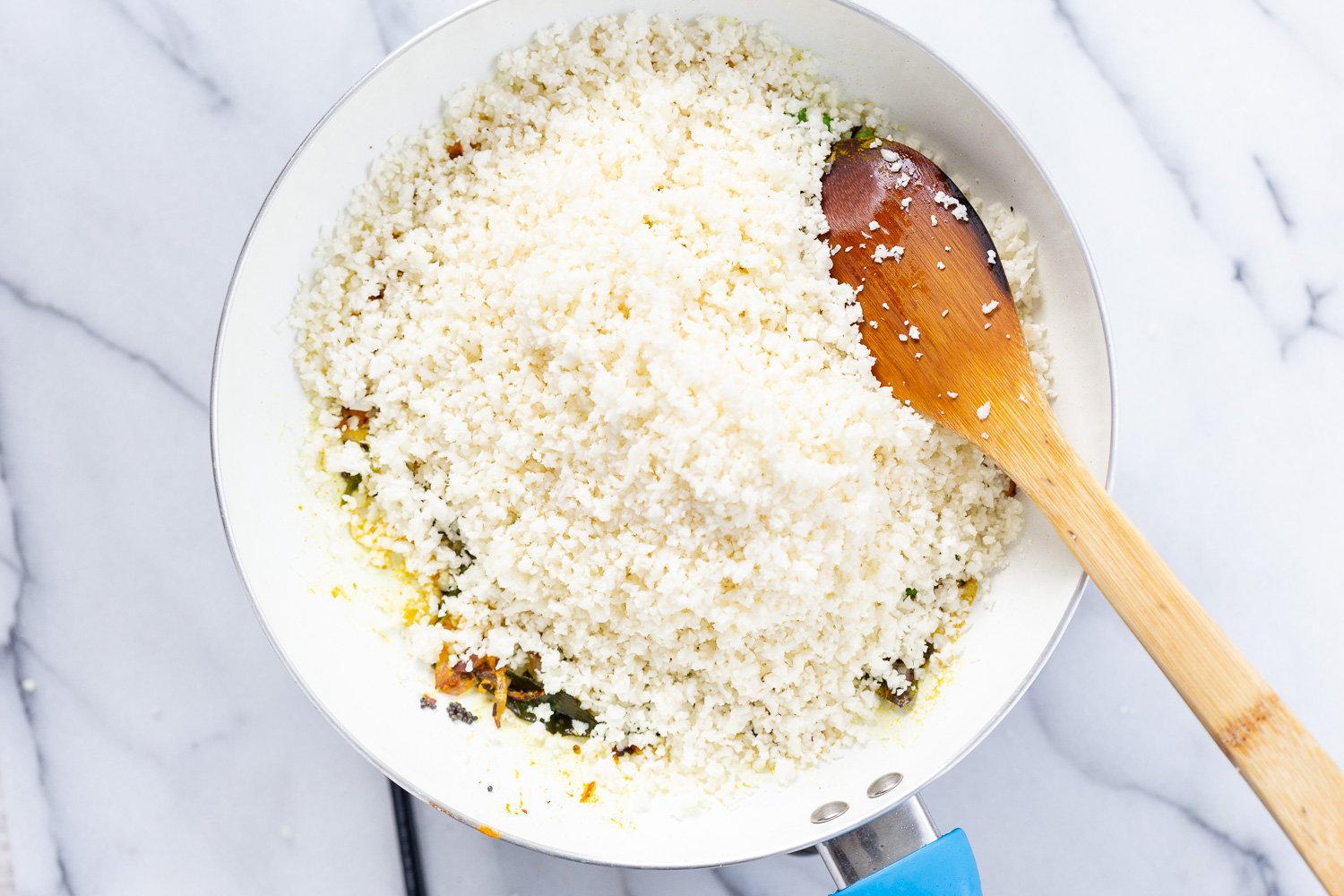 Grated Cauliflower for Our Turmeric Cauliflower Rice added to a white skillet