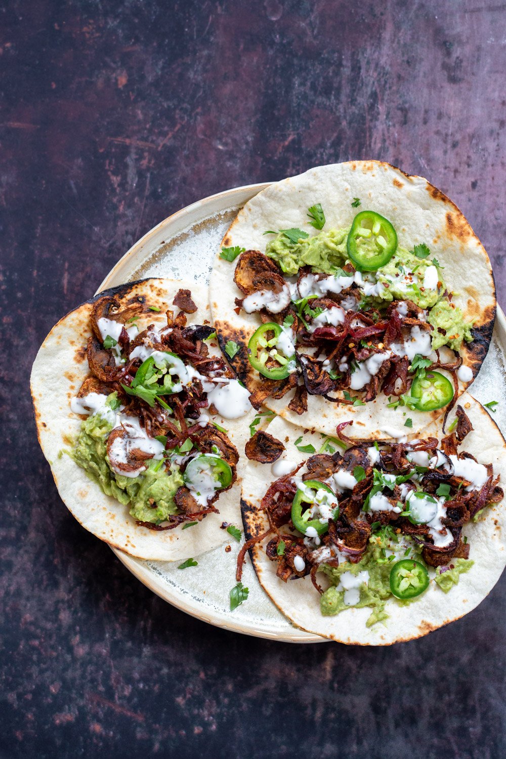 Vegan Carnitas Tacos with mushrooms, guacamole and sour cream placed in a speckled plate