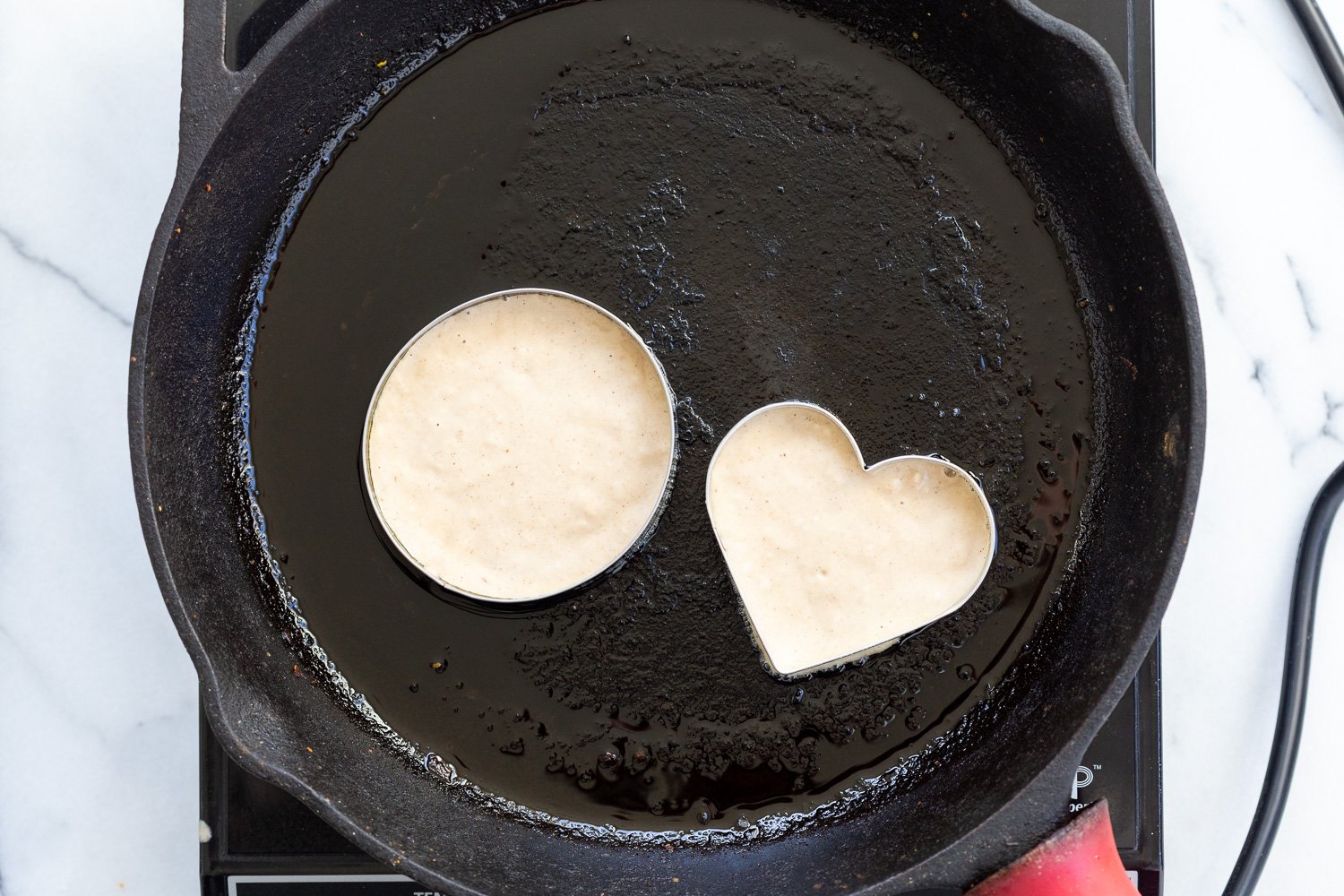Vegan Cinnamon Streusel Pancakes batter cooked in cookie cutters on a cast iron skillet