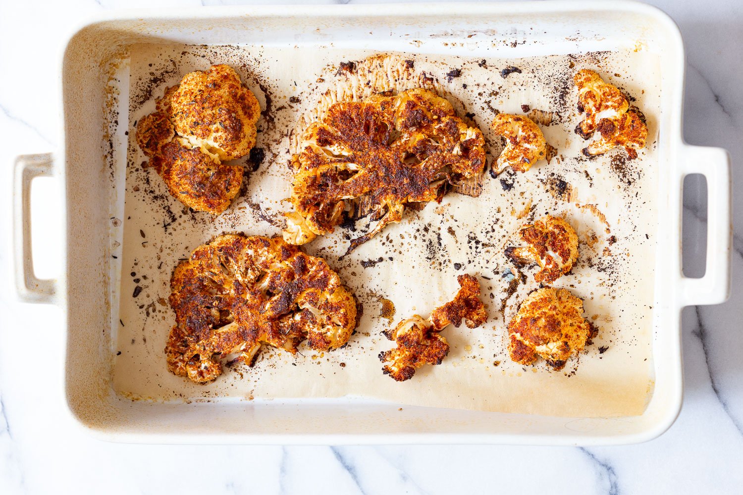 Baked Cajun Roasted Cauliflower Steaks Slices on parchment line white baking dish