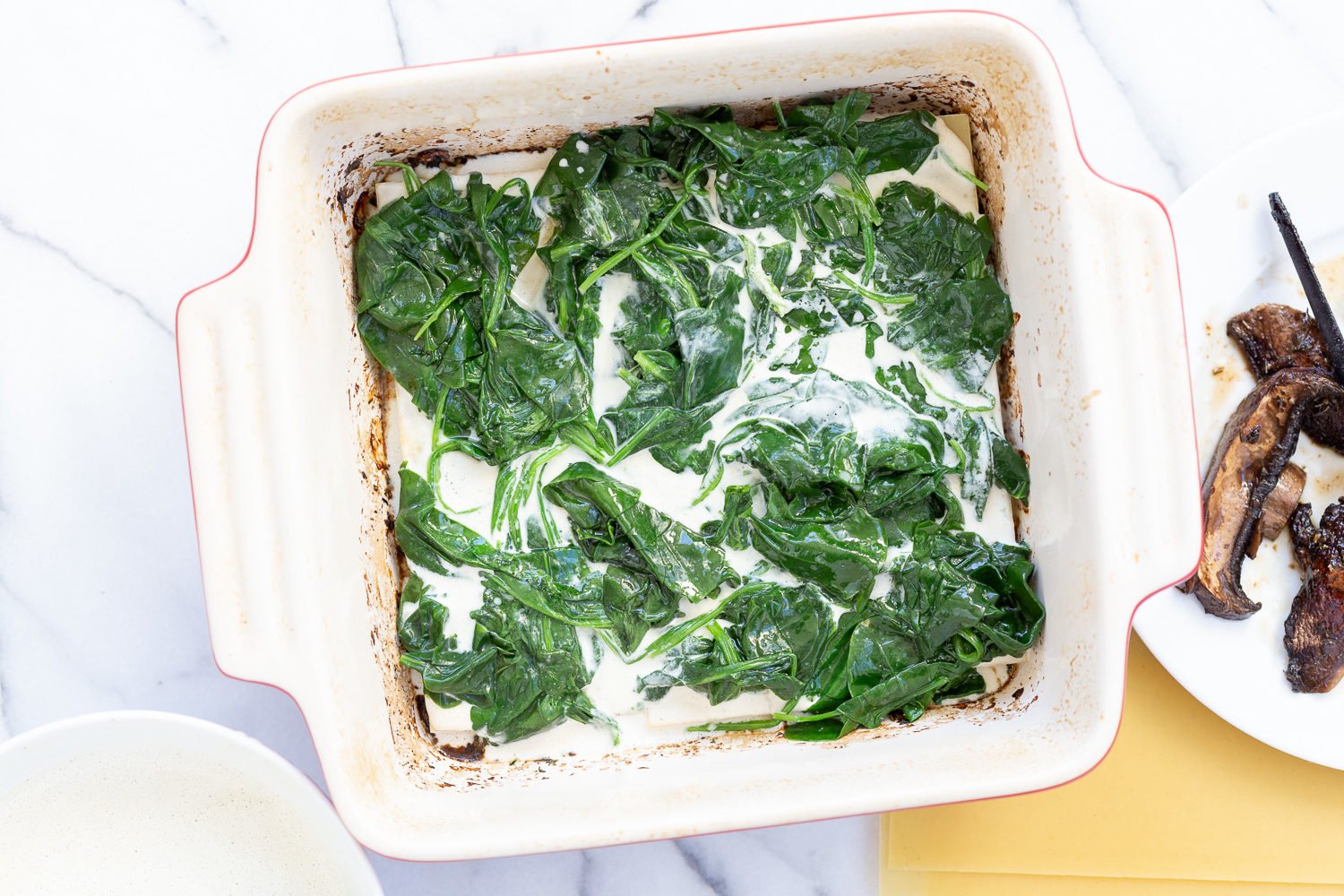 Lasagna noodles layered with spinach and garlic sauce for Our Creamy Vegan Mushroom Lasagna