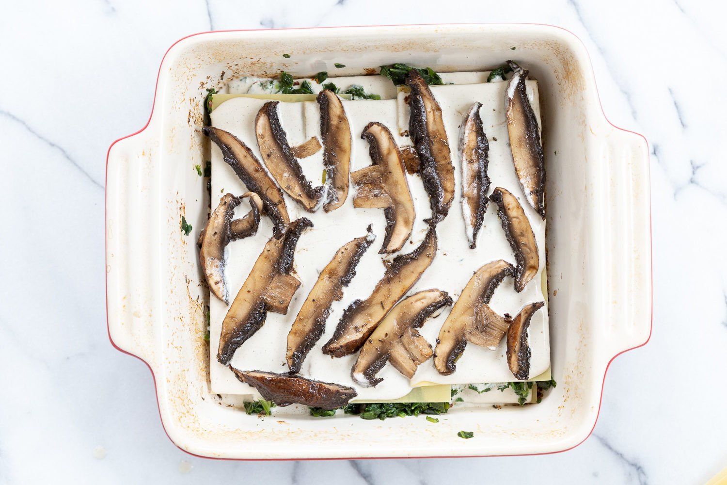 Layering steps with lasagna noodles, marinated portobello mushrooms, garlic sauce in a baking dish for Our Creamy Vegan Mushroom Lasagna