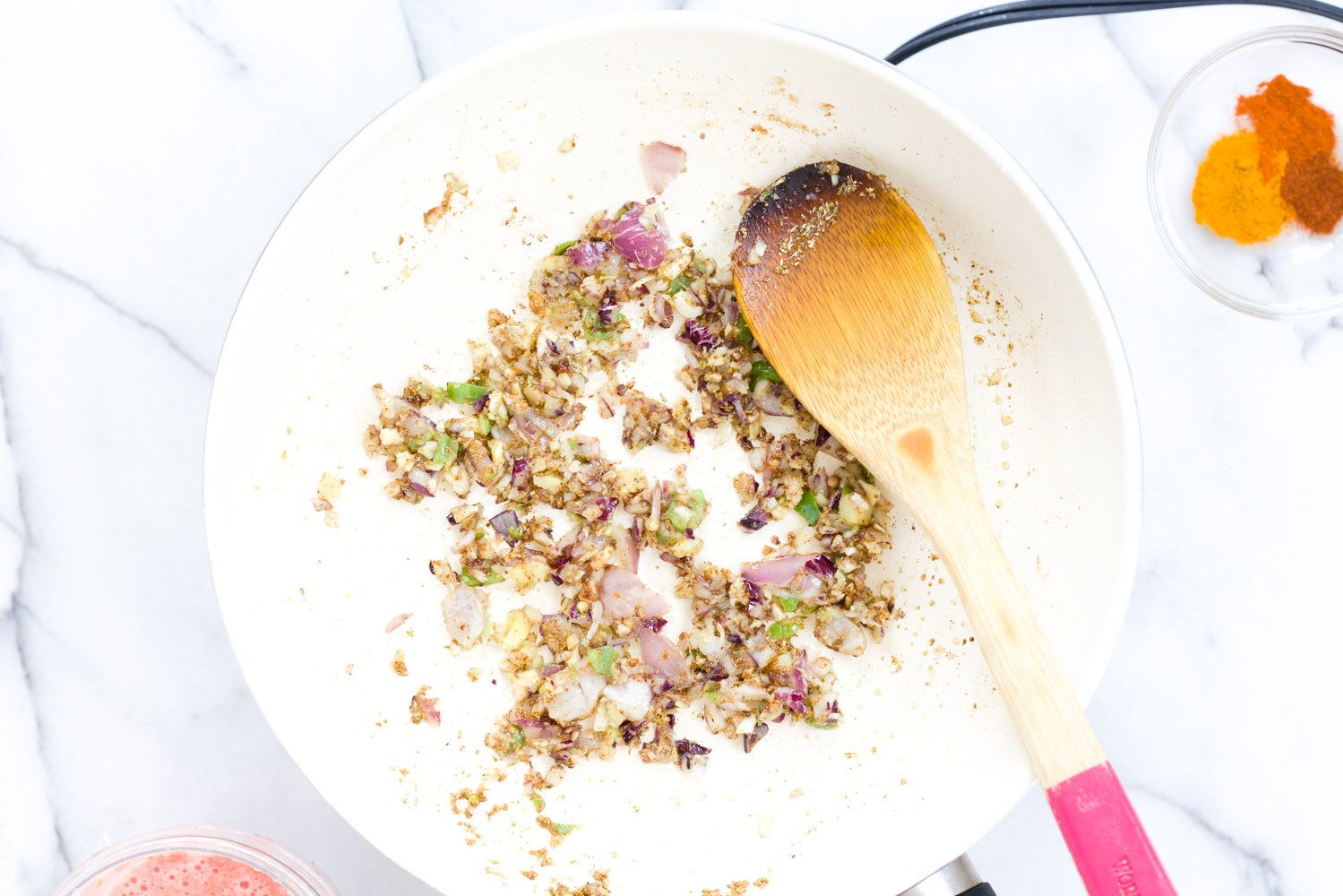 aloo matar garlic, onion and chili being added to toasted spiced in a white skillet