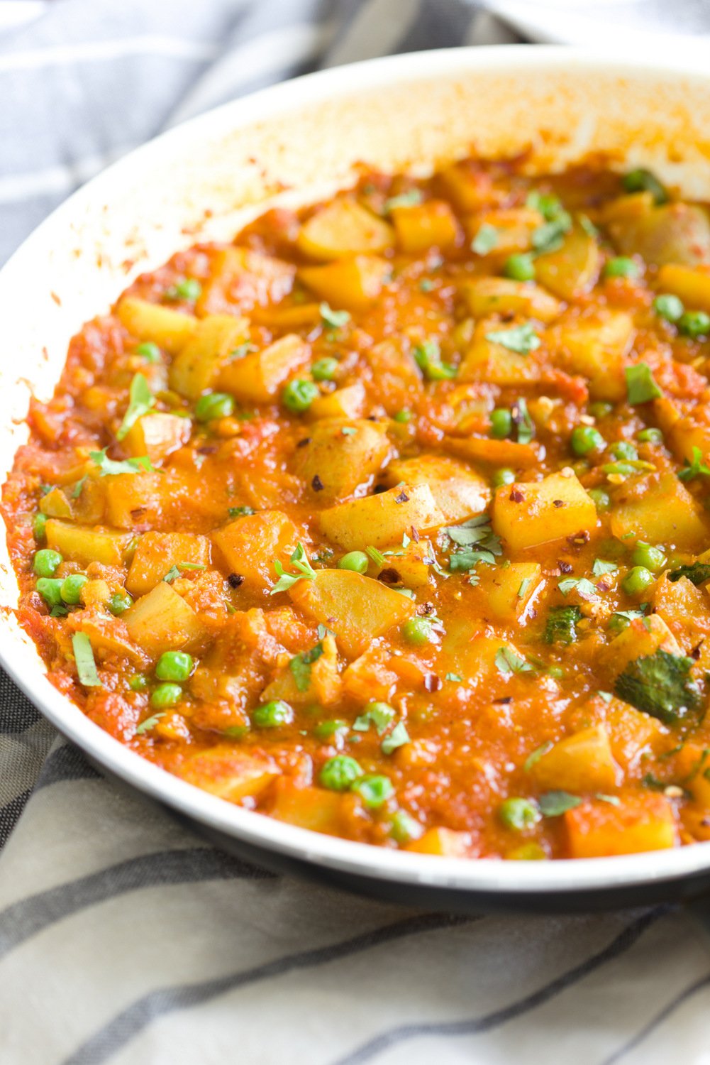 aloo matar side view of a skillet with vegan aloo matar potato pea curry