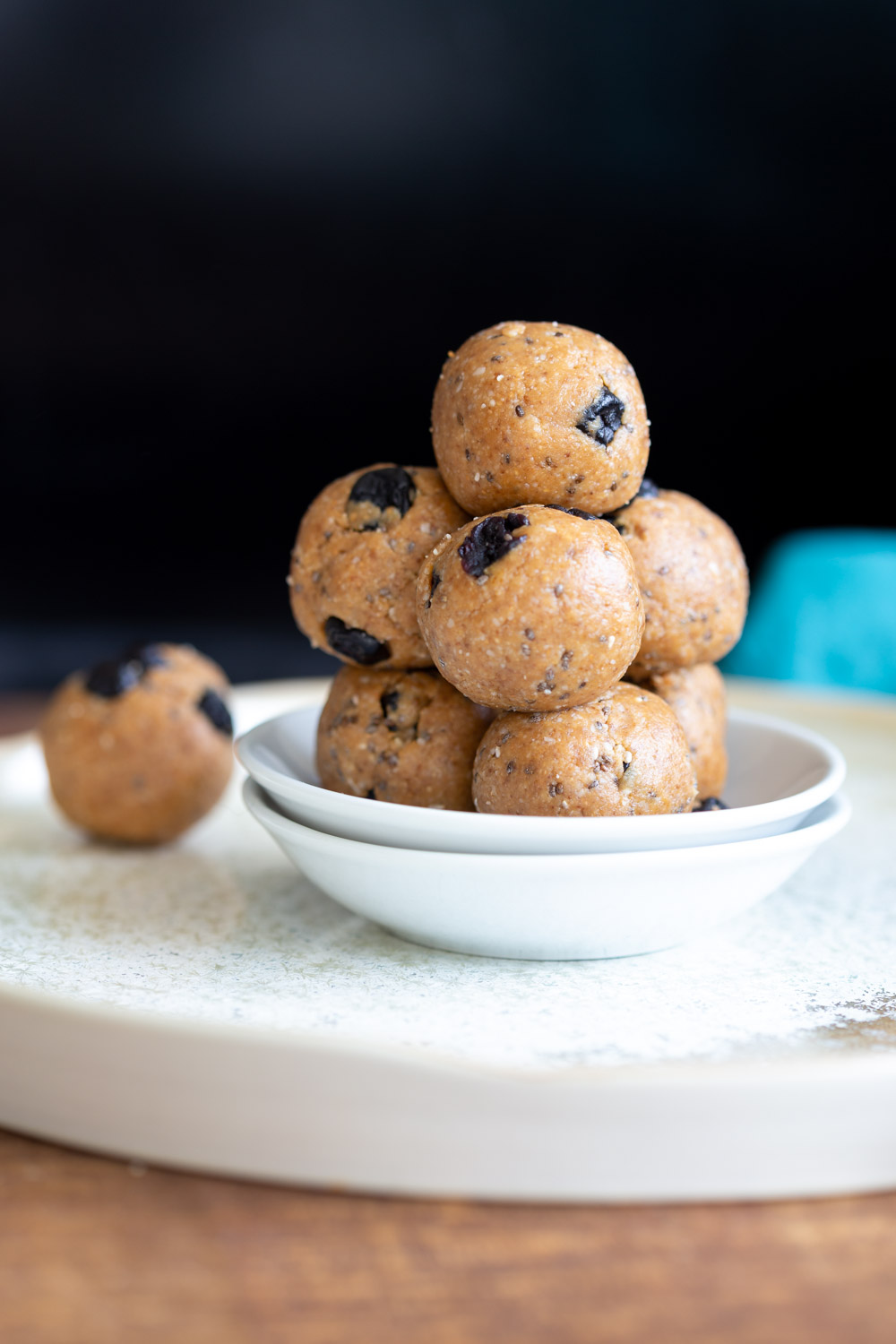 Our Vegan Blueberry Muffin Energy Bites stacked in a white plate against dark background