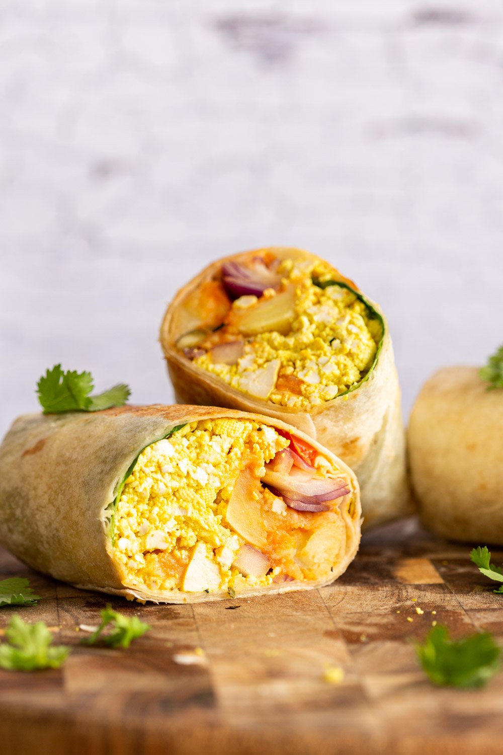 Vegan Breakfast burrito on wooden board , Vegan Breakfast Burrito with 5 Ingredient Tofu Scramble, Breakfast potatoes, chickpea pancake, tomatoes, pepitas and salsa! 23 Gm of Protein. High protein breakfast burrito or tacos. Nutfree Recipe. Can be Gluten-free, Soyfree