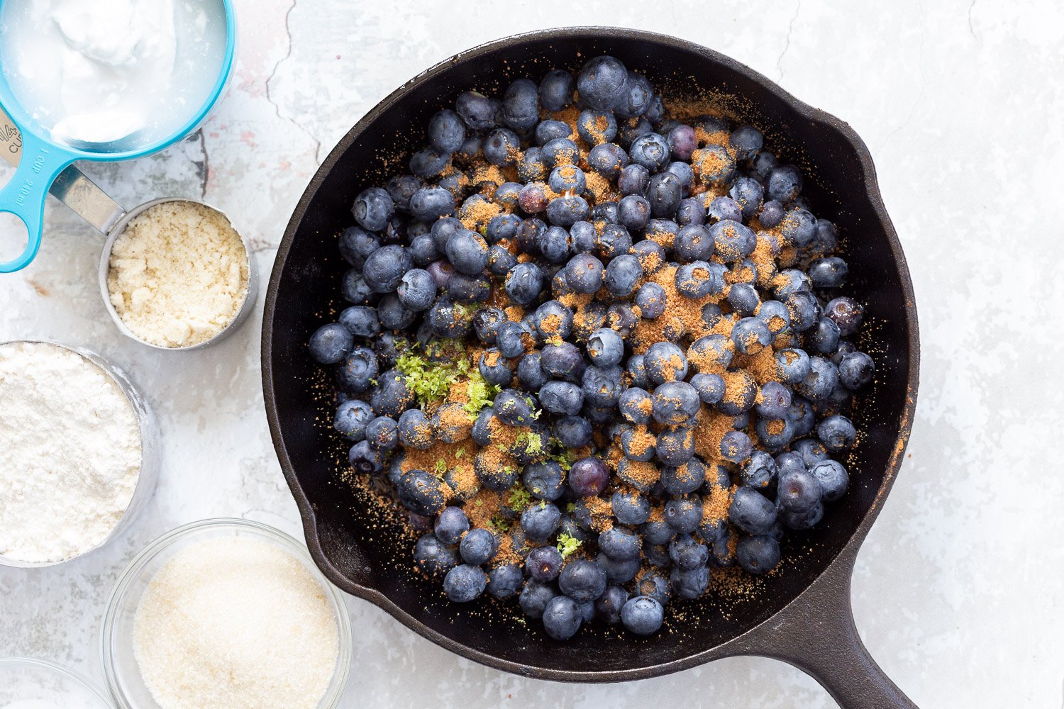 Blueberries sugar and lemon zest in cast iron skillet for our Vegan Blueberry Cobbler