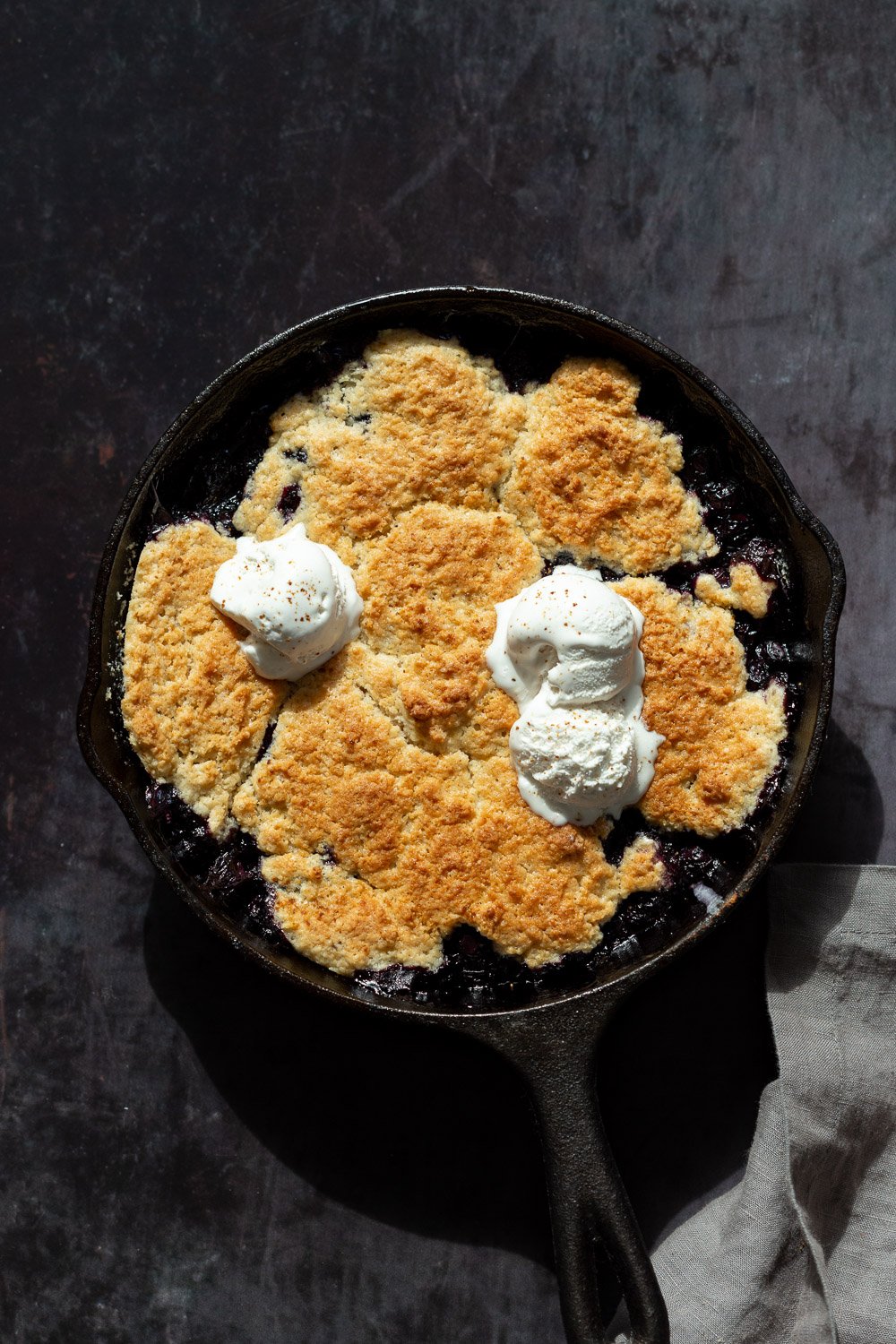 Our Vegan Blueberry Cobbler in a Cast Iron skillet over metal board
