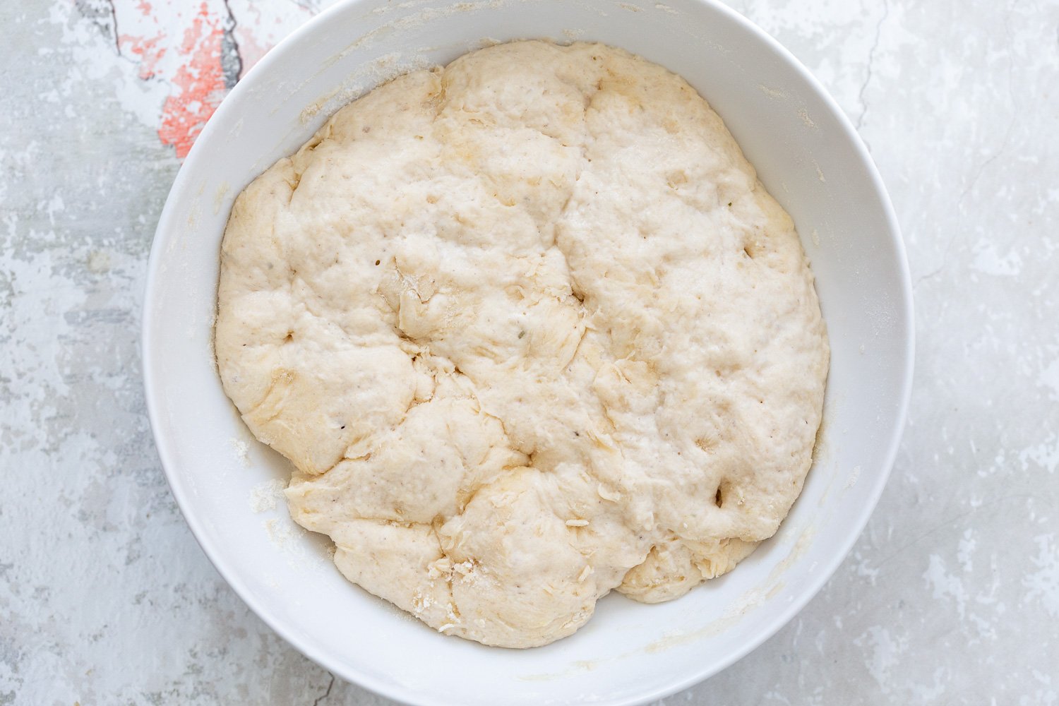 pizza rolls recipe  proofed pizza dough doubled in size sitting in a white bowl ready to be punched down