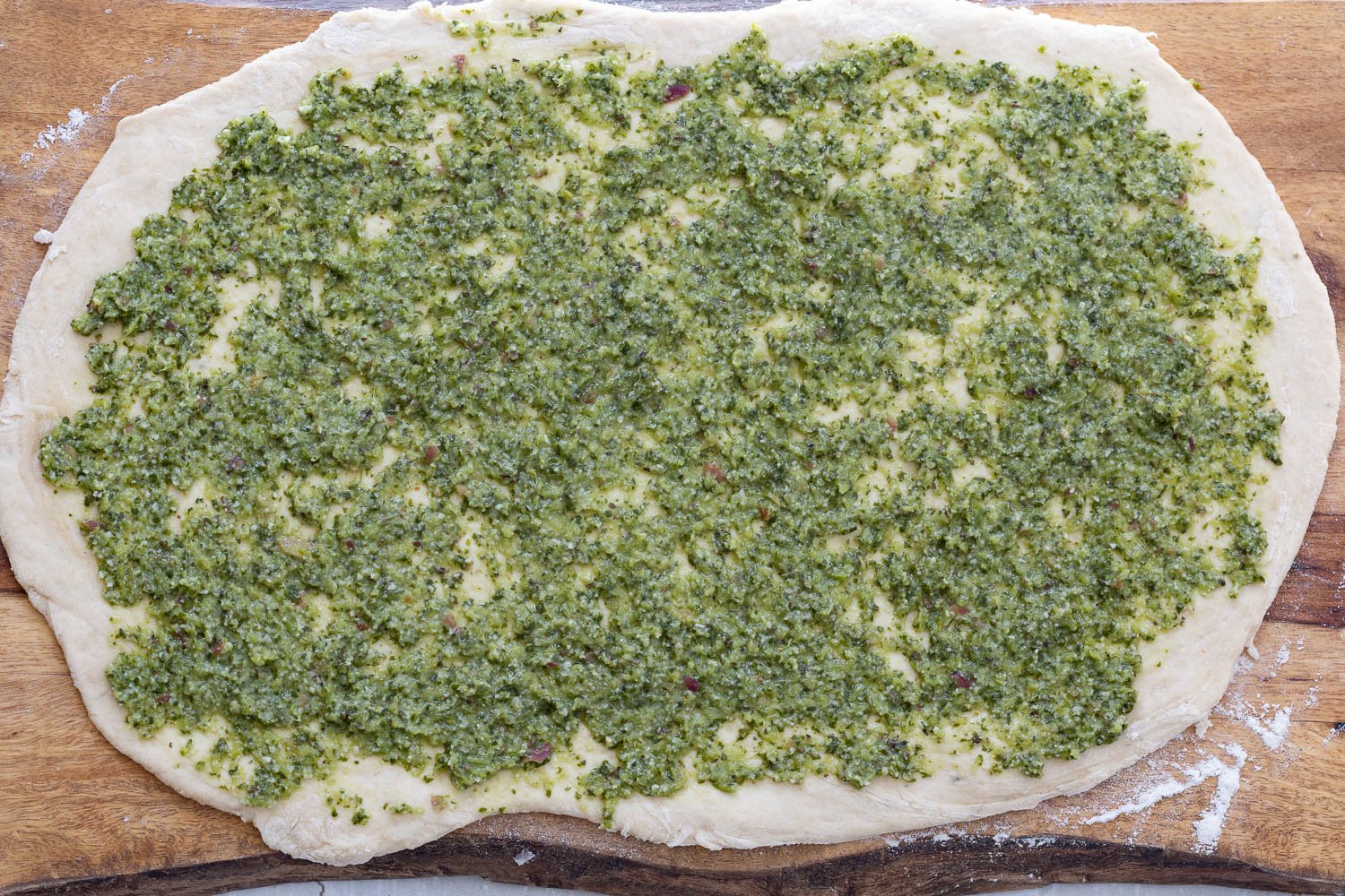 pizza rolls recipe  vegan pesto being spread onto rolled out pizza rolls dough