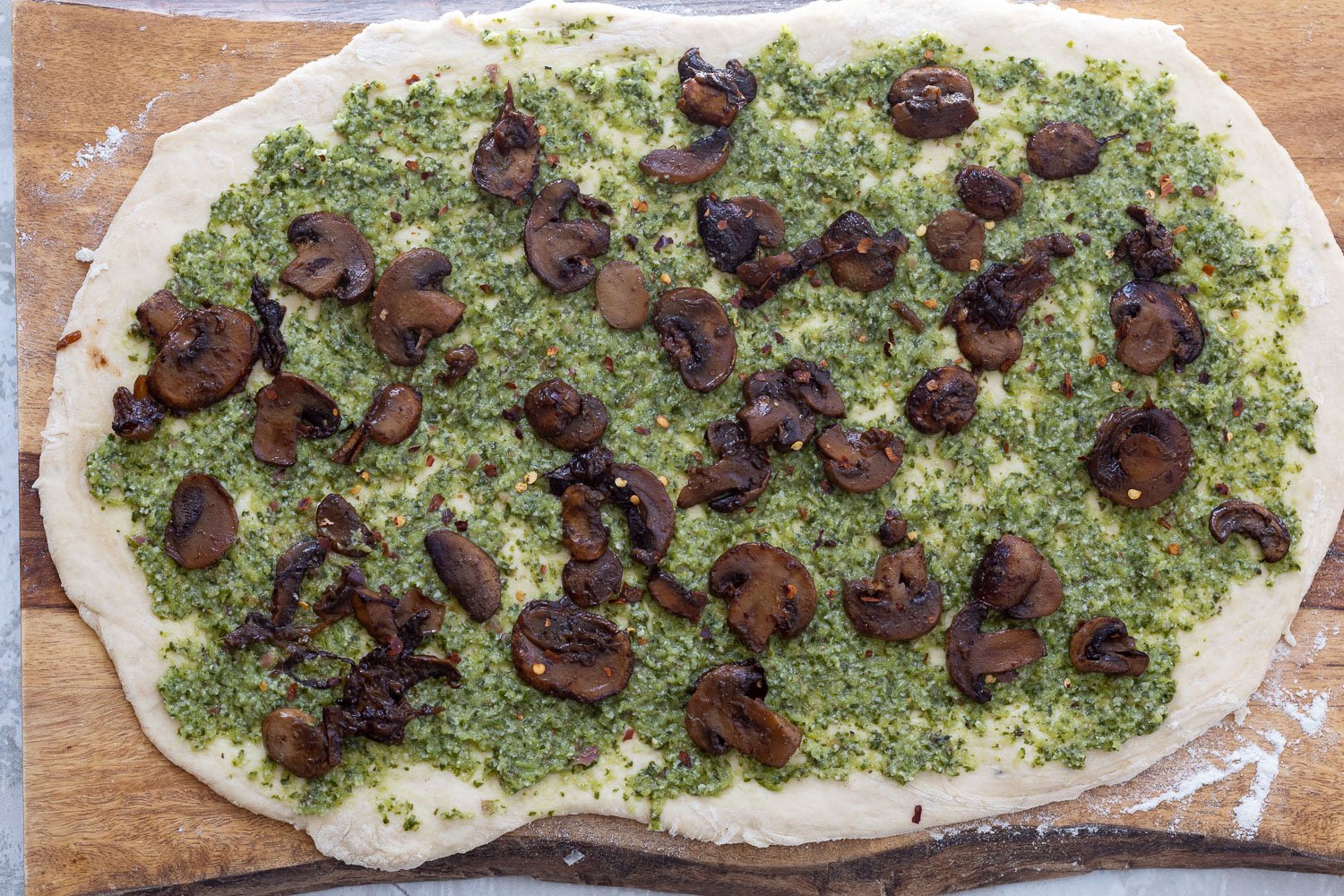 pizza rolls recipe  sauteed mushrooms being sprinkled onto rolled out pizza dough spread with pesto