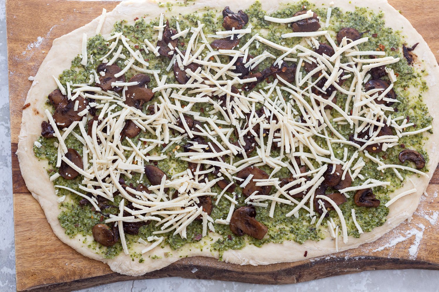 pizza rolls recipe shredded vegan mozzarella being sprinkled onto pizza dough to make pesto pizza rolls