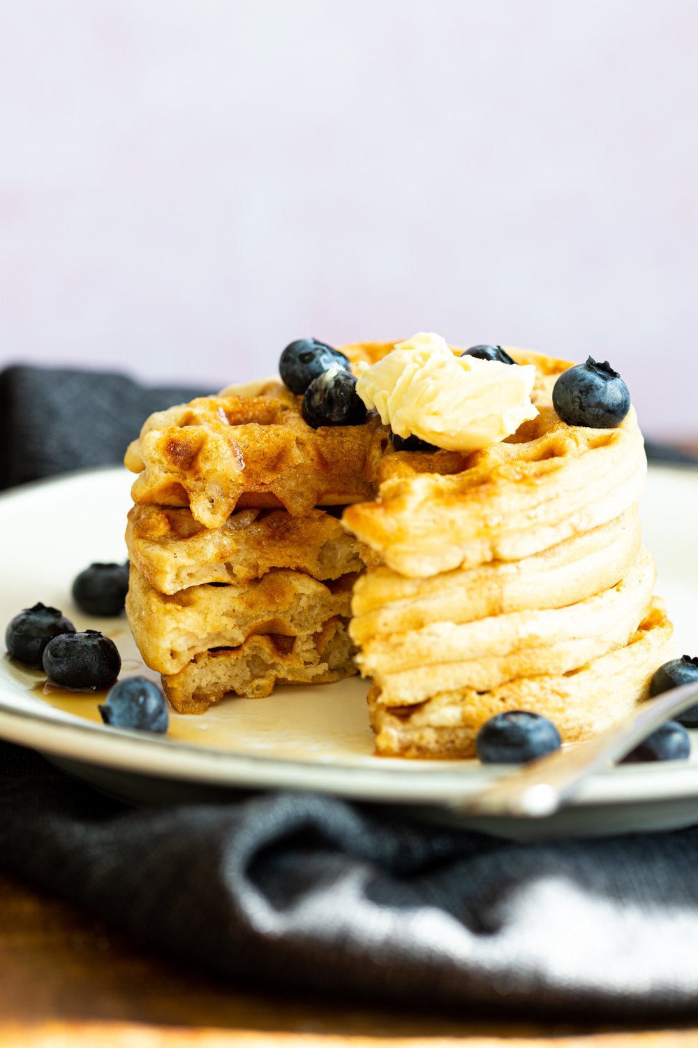 Our Easy Vegan Waffles stacked on a white plate over black napkin