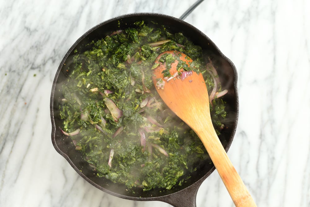 Spinach getting cooked in cast iron skillet