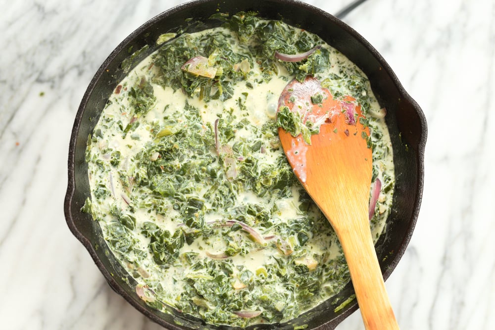 Creamy non dairy milk added to spinach in cast itron skillet