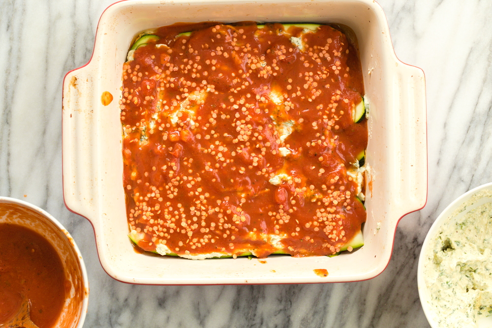 Layering Our Vegan Gluten free Zucchini Lasagna in a cream baking dish