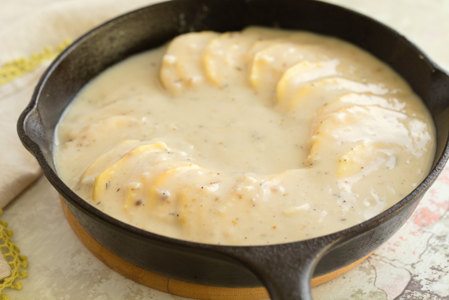 sliced potatoes drizzled with creamy cheesy sauce in a cast iron skillet