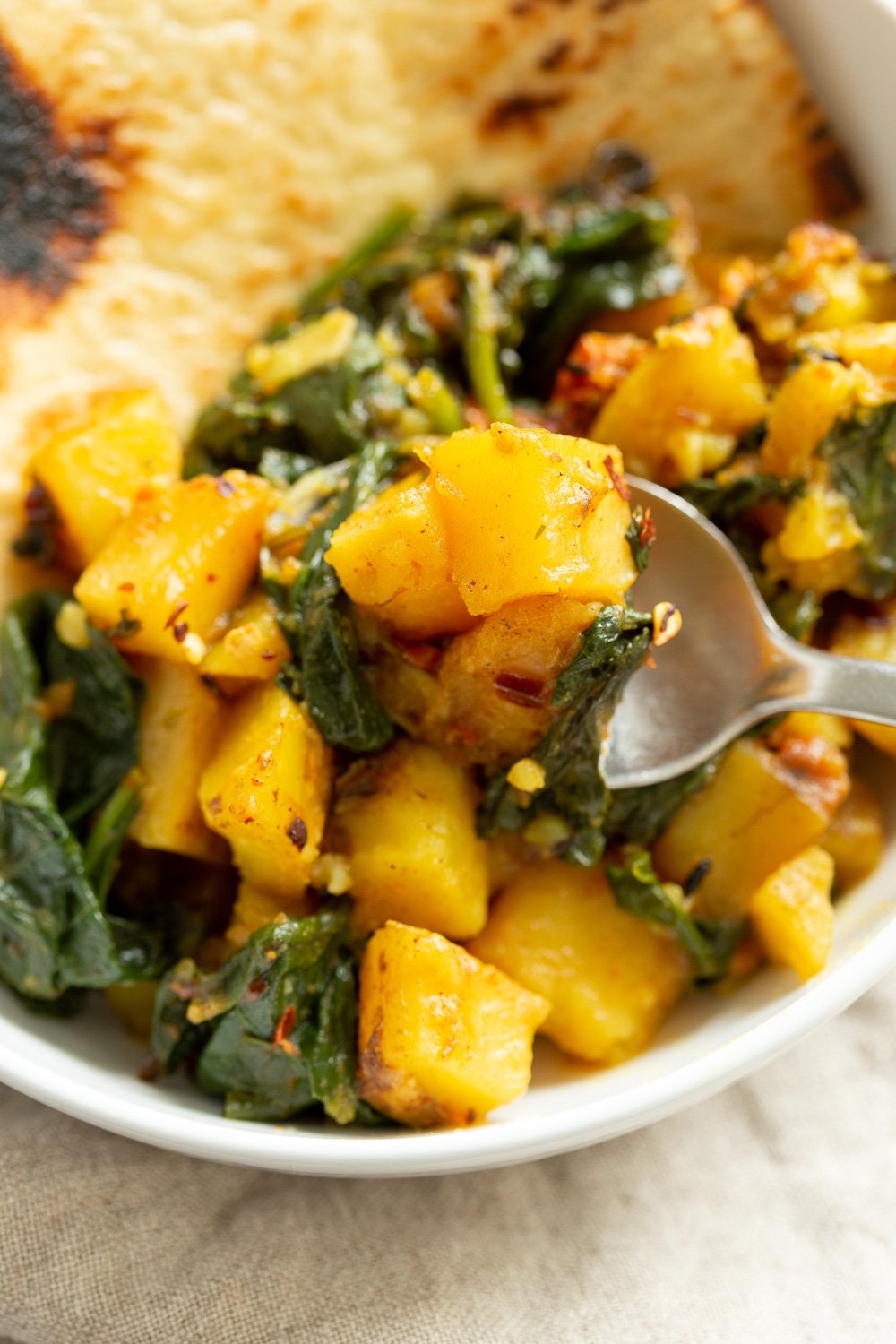 Garlic Potato Spinach Stir fry with Naan bread in a white bowl