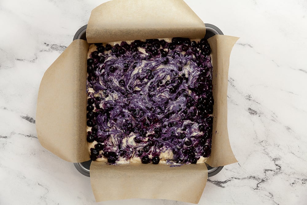 Berry Buckle Batter with blueberries in a parchment lined baking dish