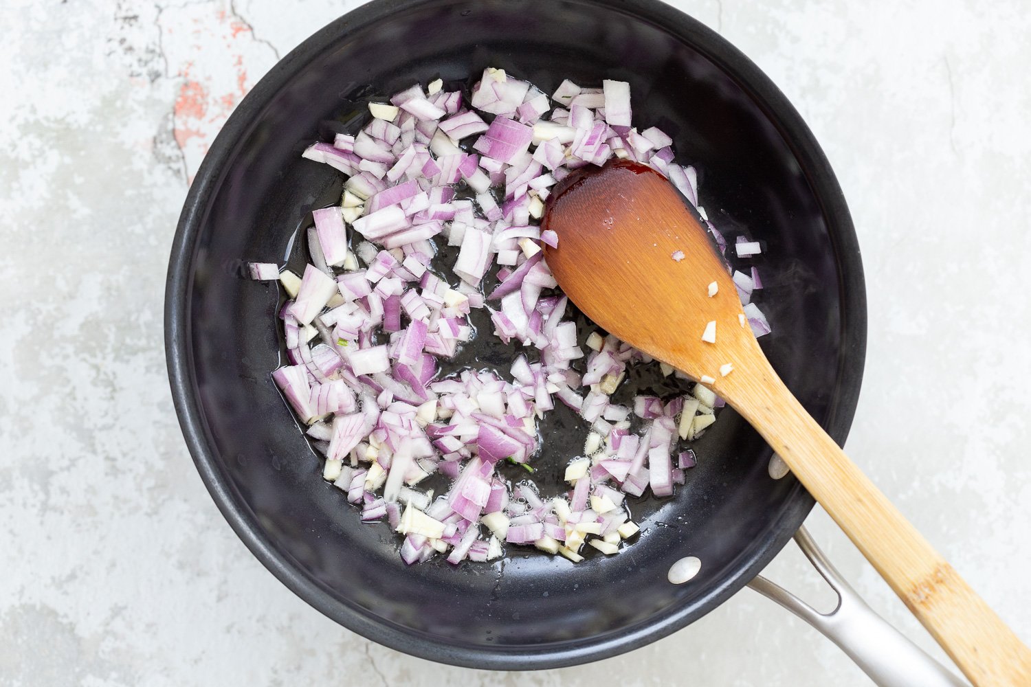 spinach pasta recipe  chopped red onions being sauteed in a black skillet