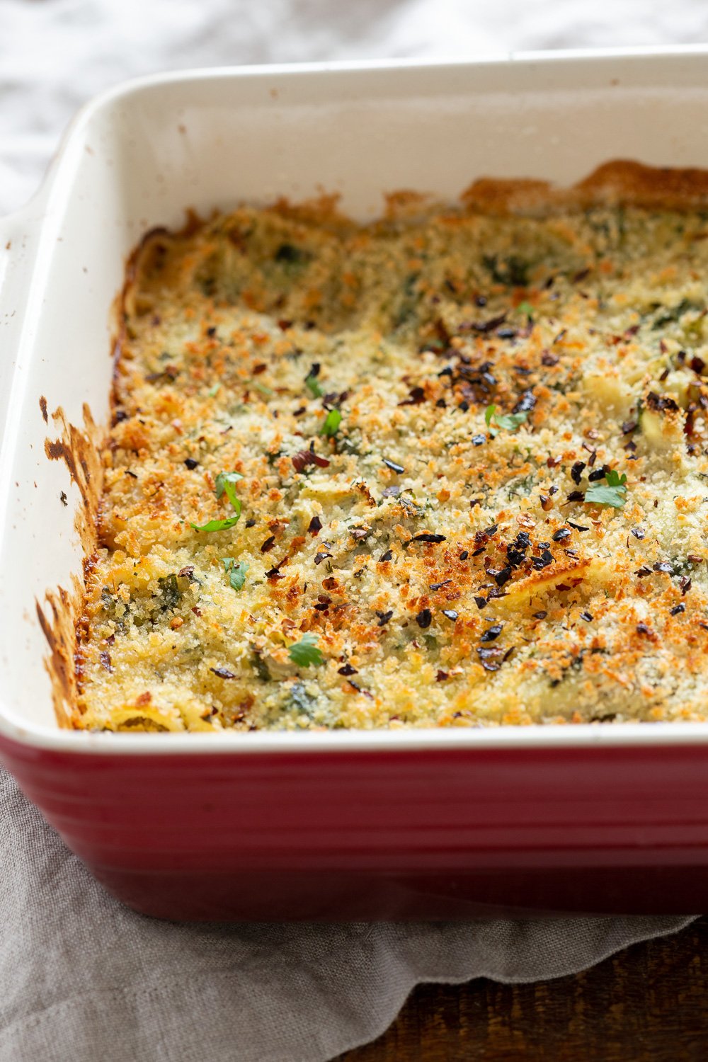spinach pasta recipe  side view close up of a red casserole dish with creamy vegan artichoke spinach pasta bake