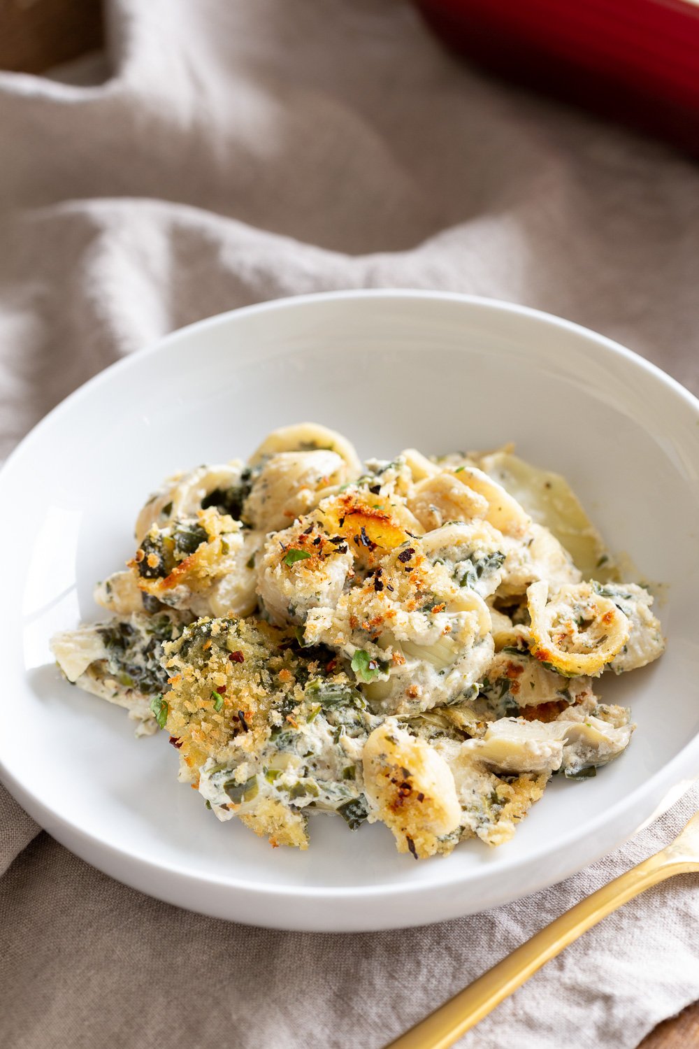 spinach pasta recipe side view of a serving of creamy vegan spinach artichoke pasta bake served in a white bowl