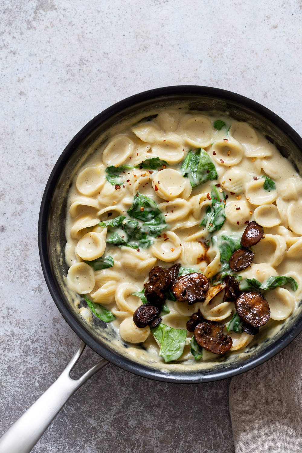 recipe for spinach pasta overhead shot of a black pot with creamy vegan spinach pasta topped with balsamic mushrooms