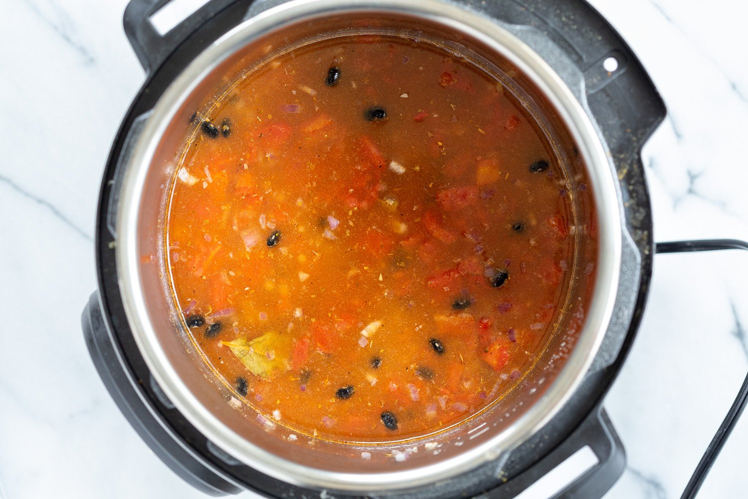 vegan black bean soup  dried soaked beans being added to an Instant Pot filled with seasoned tomato broth