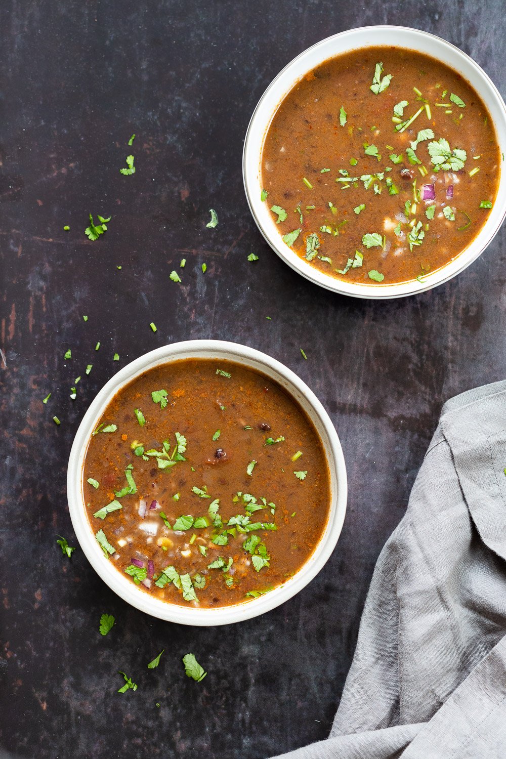 vegan black bean soup overhead shot of two bowls of vegan black beans soup sprinkled with chopped herbs