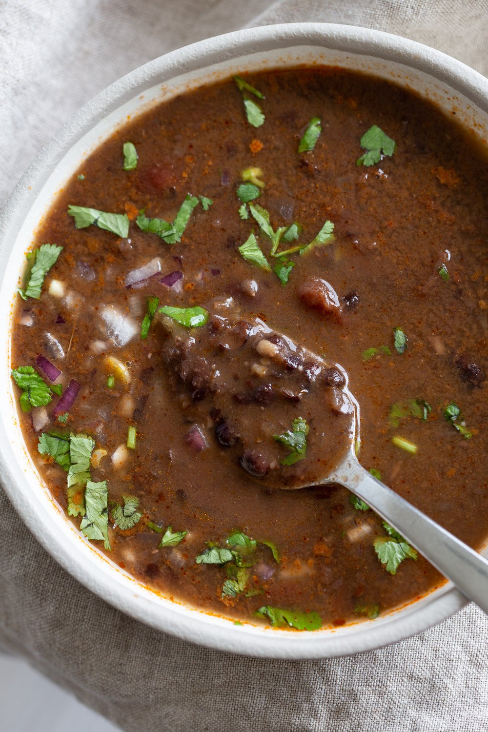 vegan black bean soup  overhead shot of a white bowl with vegan black bean soup with a spoon dipping into the bowl