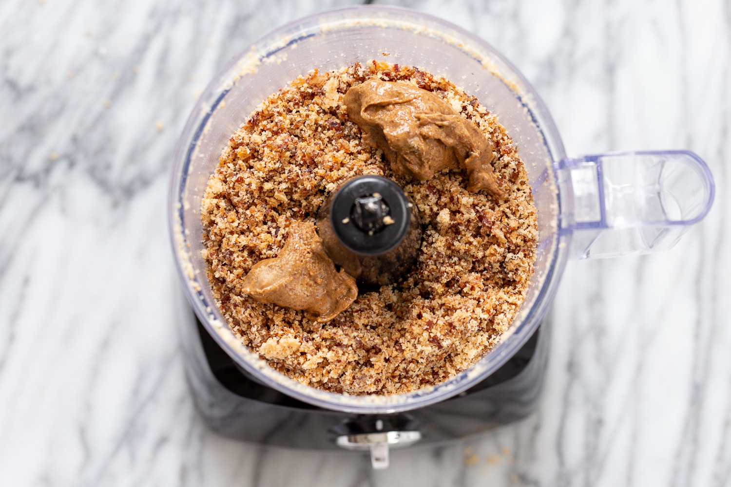 coconut balls  almond butter being added to date and coconut mixture in a food processor to make energy balls