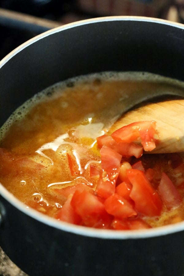 tomatoes water and spices being added to red lentils to make red lentil hummus