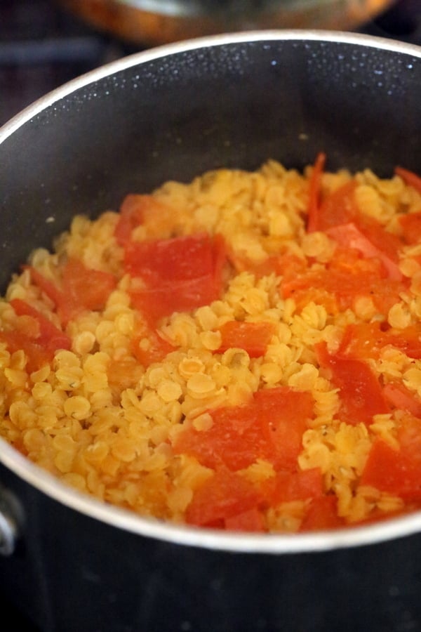 cooked red lentils and tomatoes simmering in a black saucepan to make lentil hummus