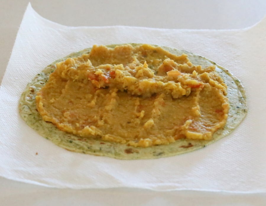 red lentil hummus being spread on top of a wheat tortilla