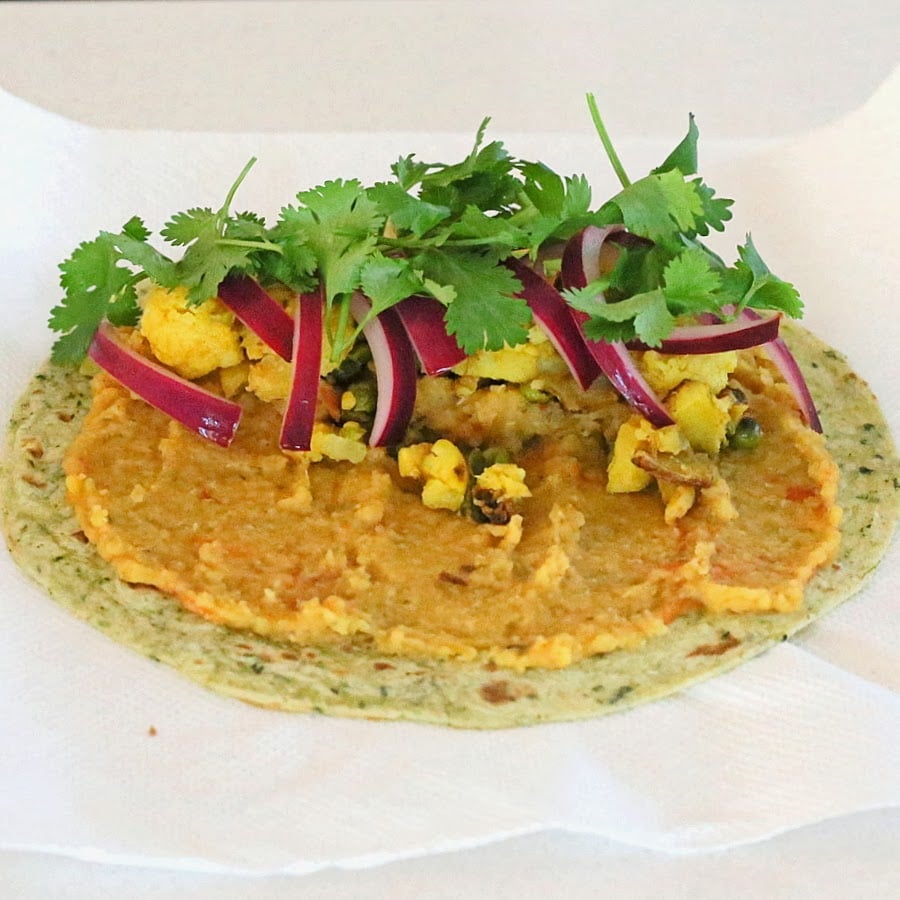 wheat tortilla topped with red lentil hummus, leftover aloo gobi, pickled onions and fresh cilantro
