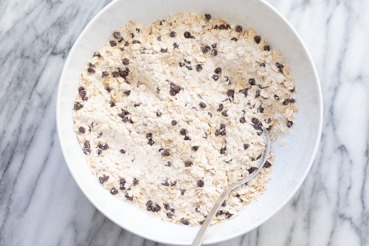 chocolate chip waffles dry ingredients for vegan oatmeal chocolate chip waffles being stirred in a white bowl