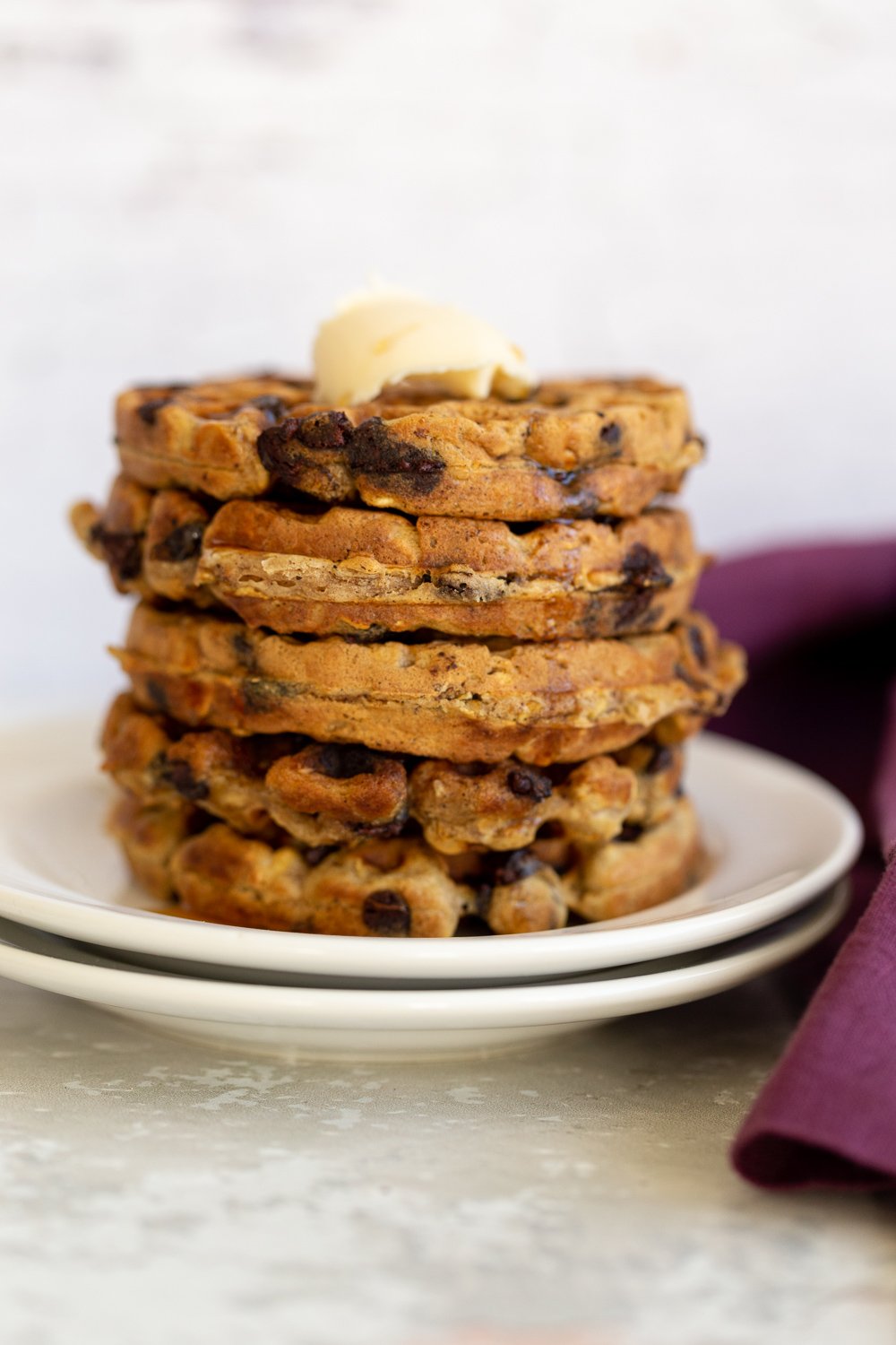 side view of a stack of vegan oatmeal chocolate chip waffles topped with vegan butter