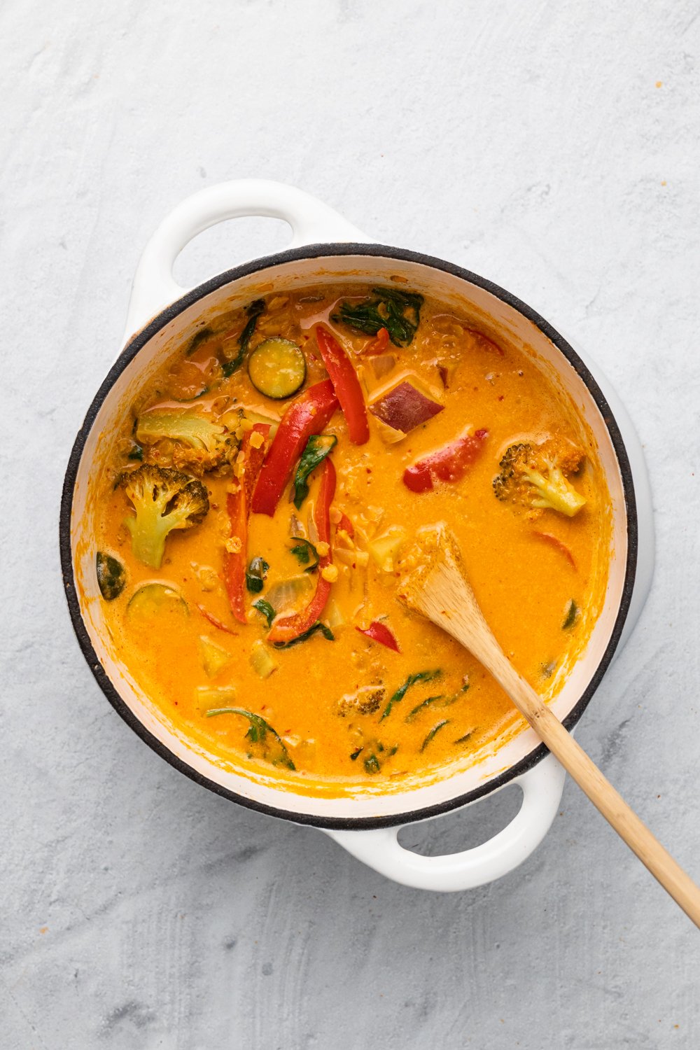 sweet potato curry  overhead shot of a pot of vegan red lentil sweet potato curry in a white pot with a wooden spoon