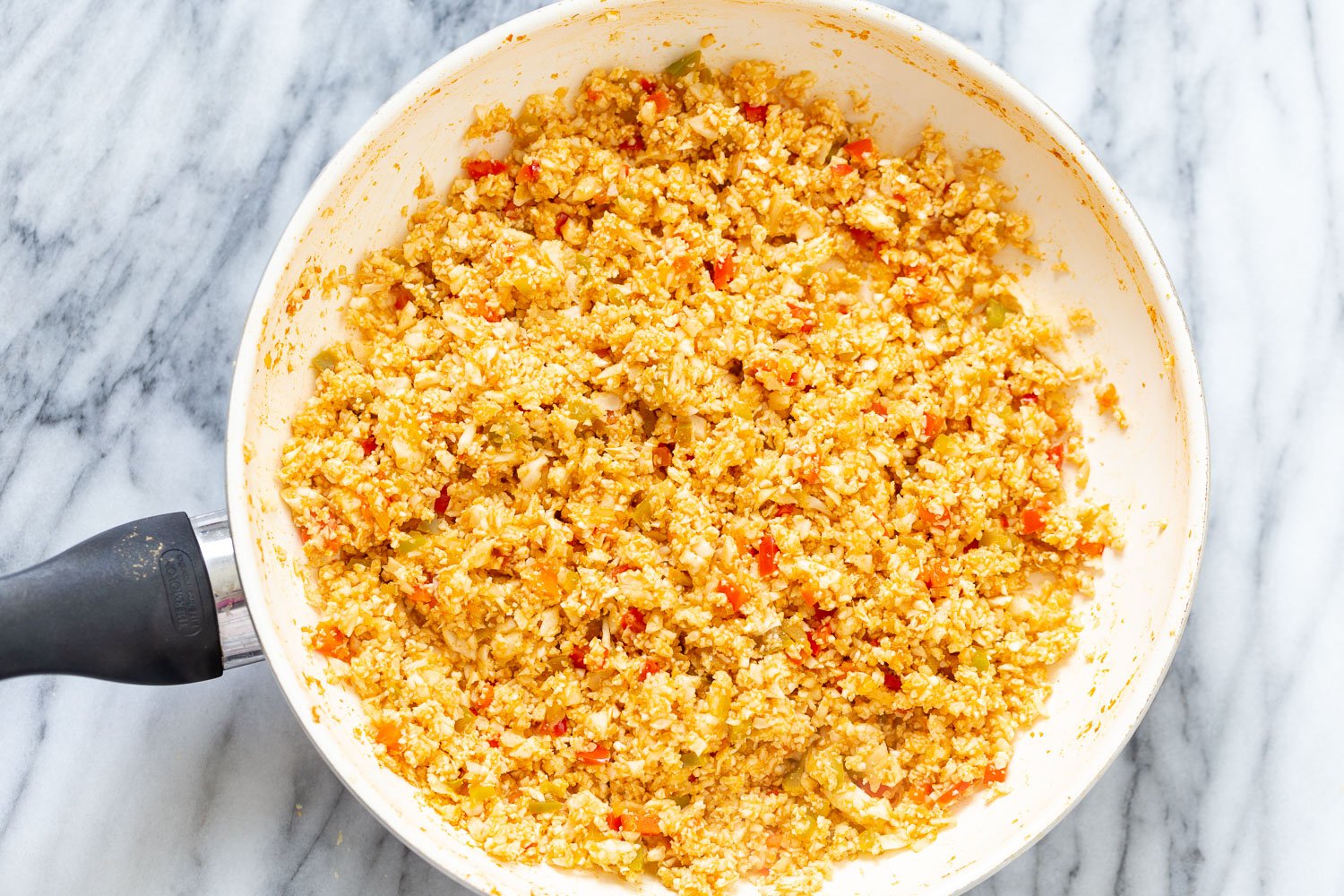 Spanish Cauliflower Rice cauliflower rice being added to a saucepan with bell pepper sauce to make Spanish Cauliflower Rice